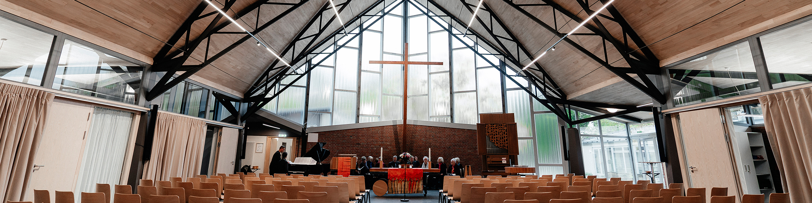 Der Gottesdienstraum der Jeremiakirche mit großer dreieckiger Glasfront. Im Altarraum schwebt ein großes Kreuz.