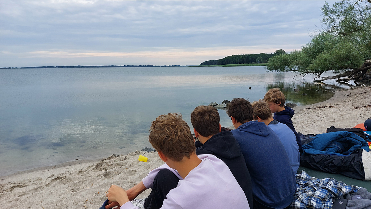 Jugendliche sitzen am Strand und schauen aufs Meer.