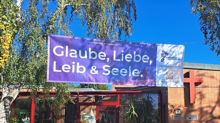 Lila Banner vor dem Gemeindehaus gespannt: Glaube, Liebe, Leib & Seele