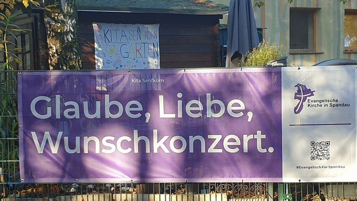 Lila Banner am Zaun: Glaube, Liebe, Wunschkonzert.