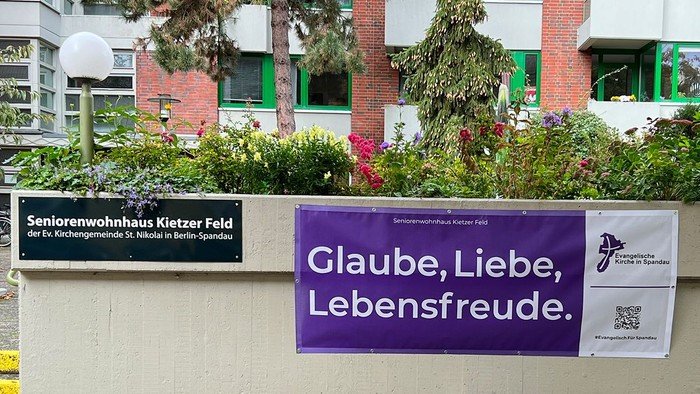 Lila Banner an der Mauer: Glaube, Liebe, Lebensfreude.