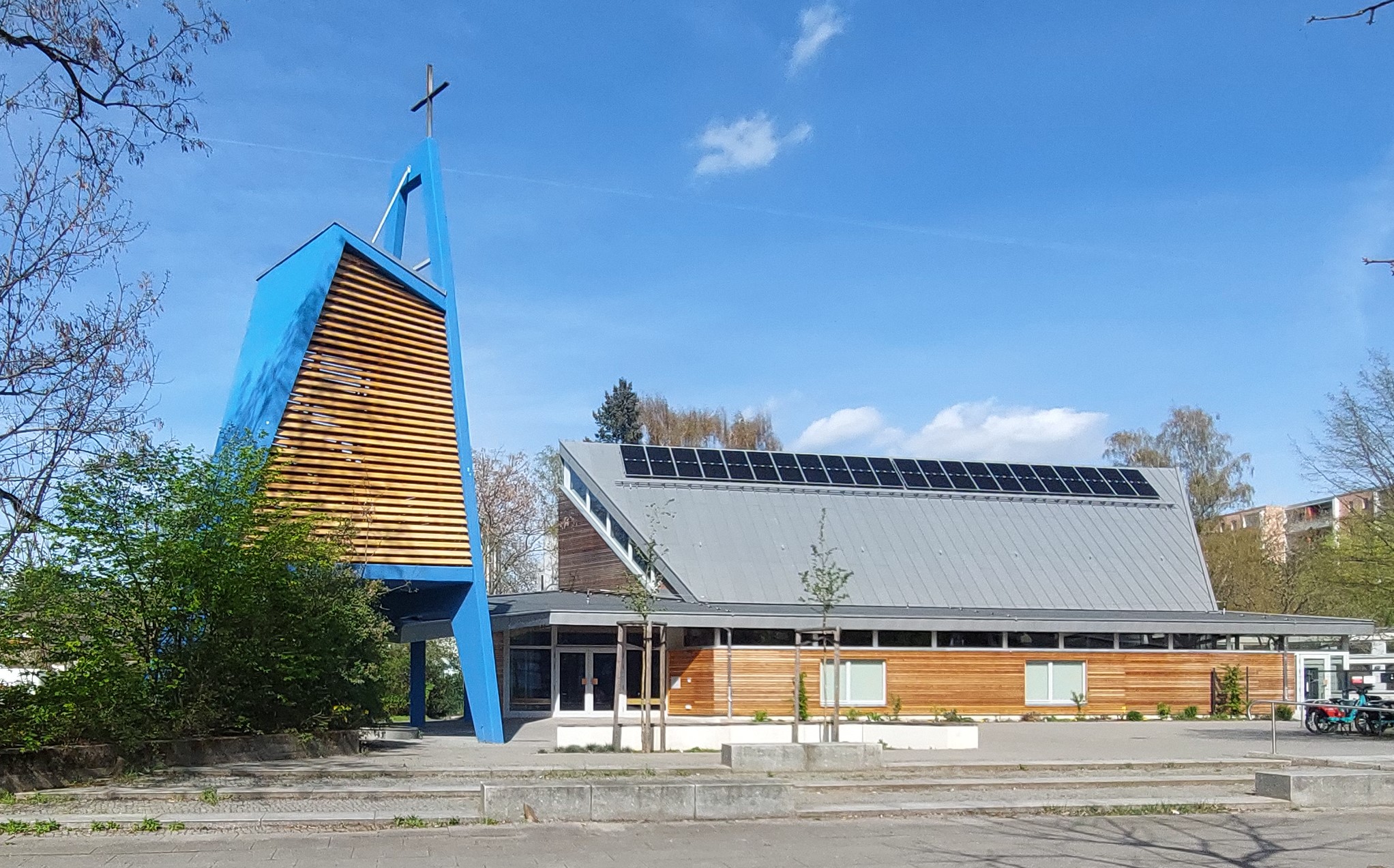 Jeremiakirche mit freistehendem Glockenturm, holzverkleidetem Erdgeschoß und Pultdach mit Solarzellen