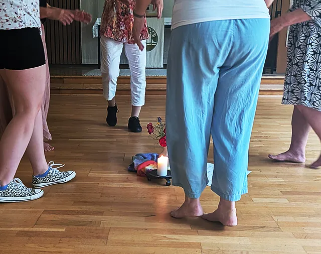 Frauen im Kreis laufen auf gestaltete Mitte mit Blumen, Kerze und Tuch zu