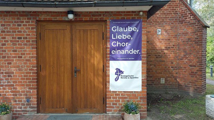 Lila Banner am Gebäude: Glaube, Liebe, Choreinander.