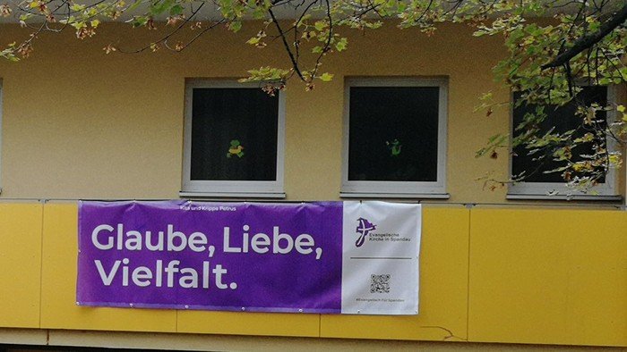 Lila Banner am Zaun: Glaube, Liebe, Vielfalt