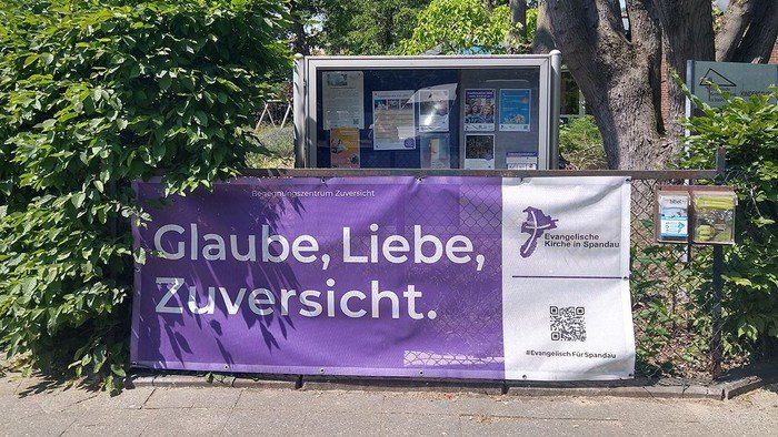 Lila Banner am Zaun: Glaube, Liebe, Zuversicht.