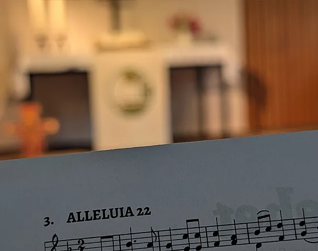 Liedzettel "Alleluia" vor unscharfem Hintergrund mit Altar