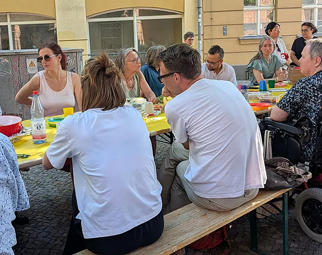Menschen unterschiedlichen Alters sitzen an Biertischen, eine Person sitzt im Rollstuhl