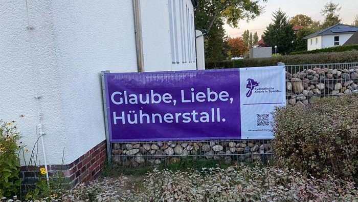 Lila Banner neben Gebäude: Glaube, Liebe, Hühnerstall.