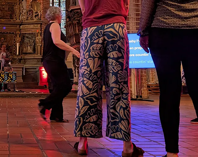 Personen stehen und tanzen vor Screen, im Hintergrund DJ und Techniker vor dem geschnitzten Altar in der St. Nikolaikirche