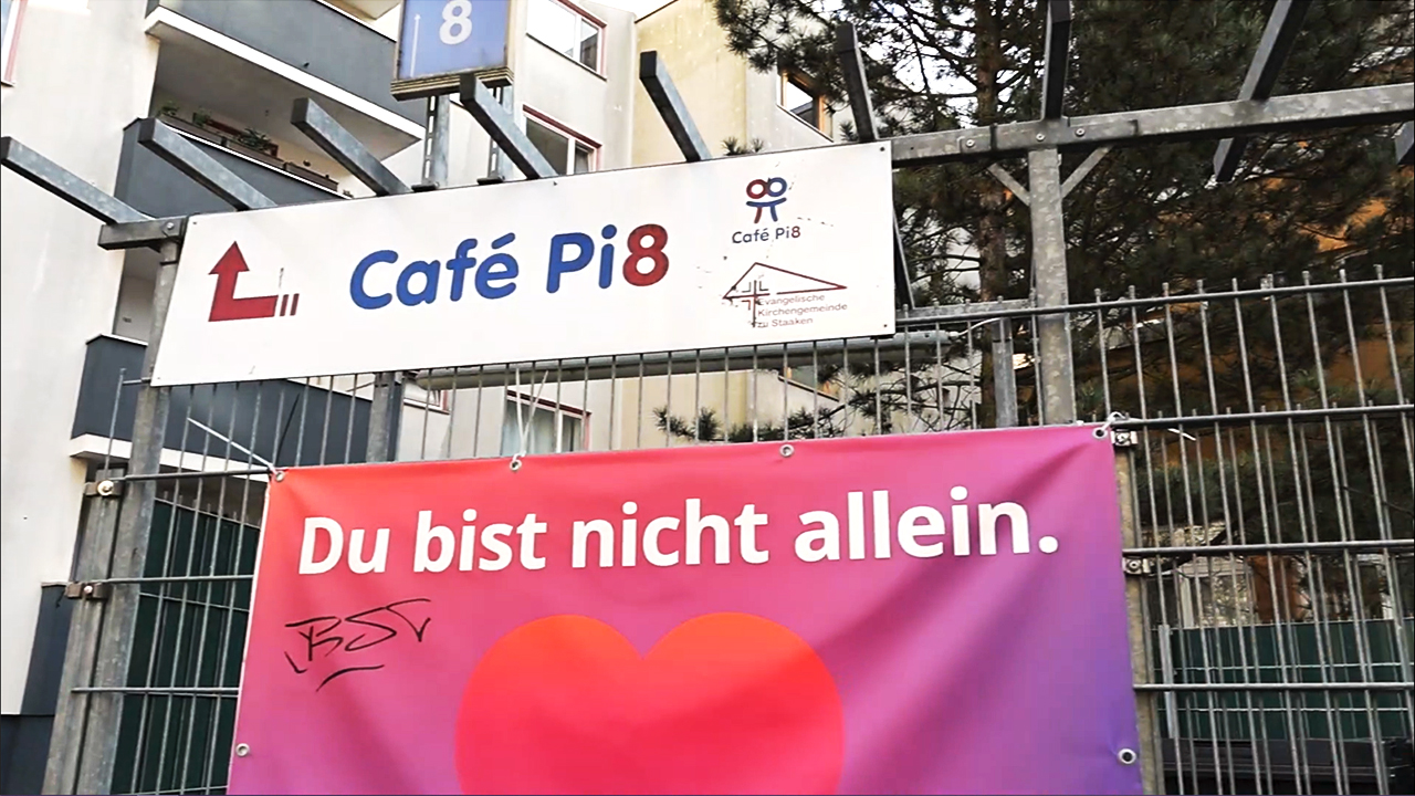 Zaun mit Schild "Café Pi8" und Banner "Du bist nicht ein allein." mit Herz