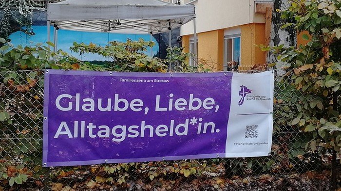 Lila Banner an Zaun: Glaube, Liebe, Alltagsheld*in.