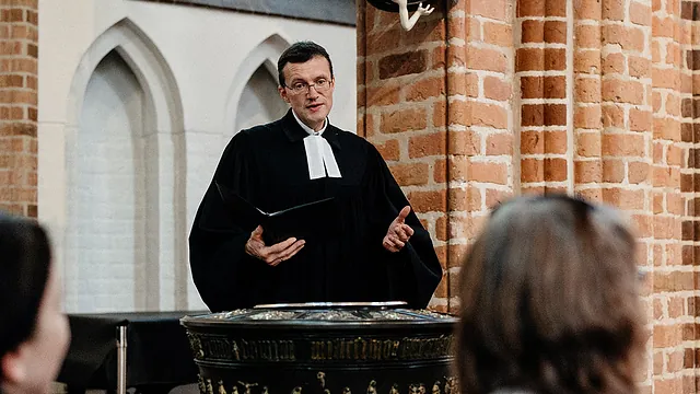 Pfarrer Thomas Martschink im Talar am Taufstein