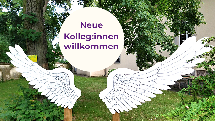 Schild "Neue Kolleg:innen willkommen" zwischen zwei Engelsflügeln.
