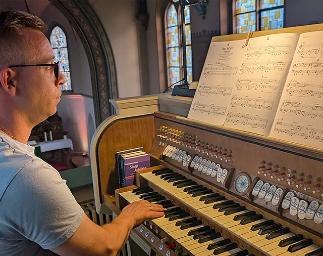 Mann spielt Orgel, im Hintergrund Kirche mit Buntglasfenstern