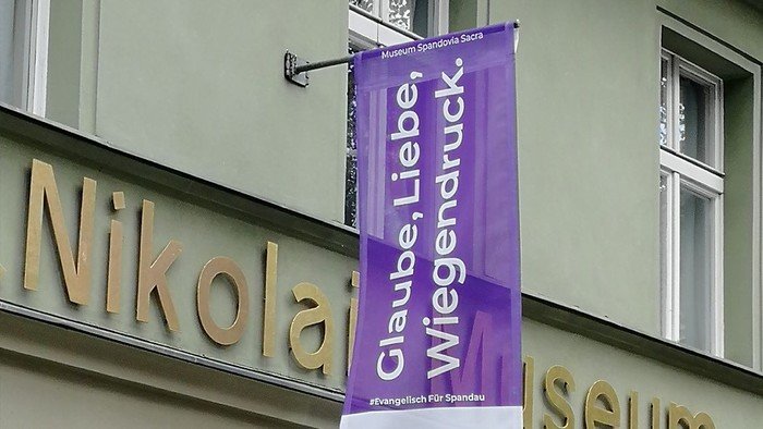 Lila Banner hängt am Gebäude: Glaube, Liebe, Wiegendruck