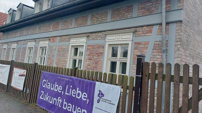 Lila Banner am Zaun: Glaube, Liebe, Zukunft bauen.