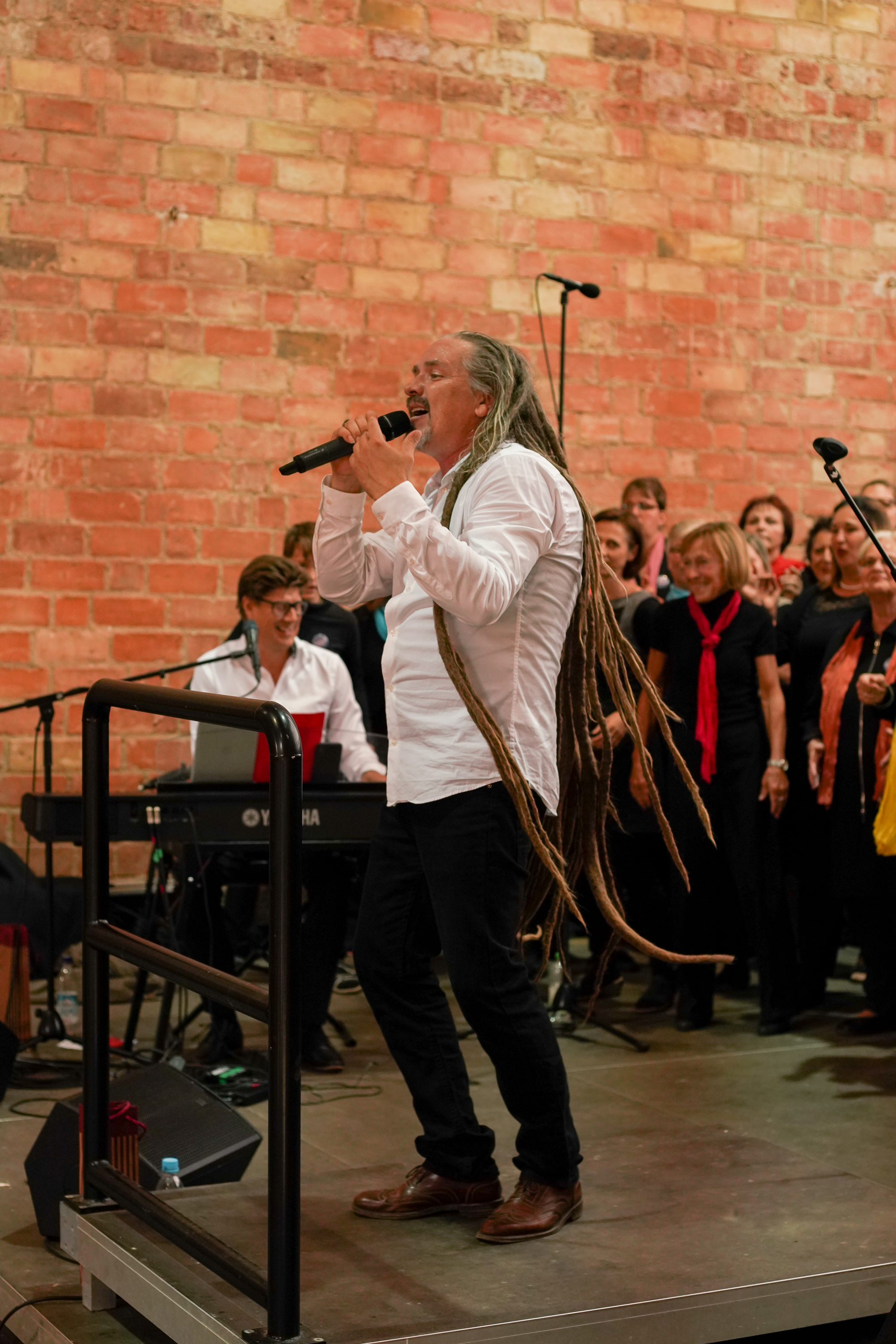 Ein Sänger mit langen Dreads sind vor einem Chor.