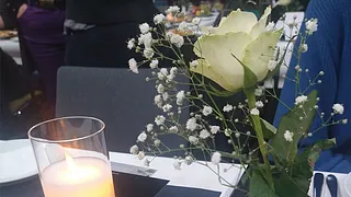 Gedeckter Tisch mit brennender Kerze, weißer Rose in Vase.
