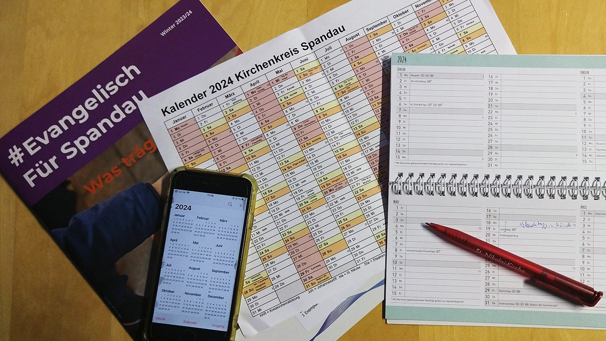 Magazin #Evangelisch Für Spandau, eine Jahresübersicht vom Kirchenkreis, ein Bürokalender, ein Handy und ein Kugelschreiber liegen auf einer Fläche