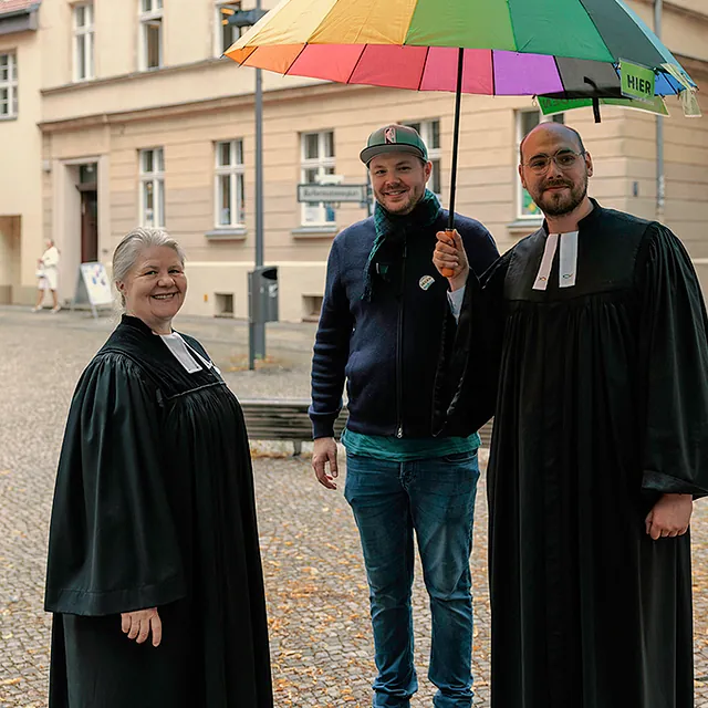 Pfarrerin Leukert, Popchorleiter Seidel und Pfarrer Herzer unterm Regenbogenschirm