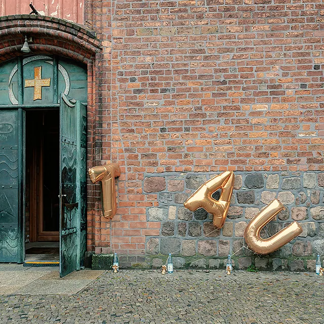 Offenes Portal St. Nikolai, vor der Steinwand goldene Buchstaben-Folienballons TAUF
