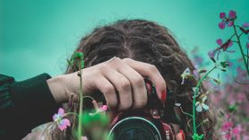 Eine Frau fotografiert mit einer Kamera zwischen Blumen hindurch.