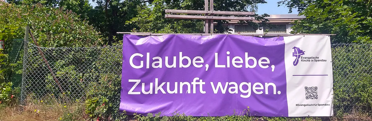 Lila Banner "Glaube, Liebe, Zukunft wagen." an Zaun