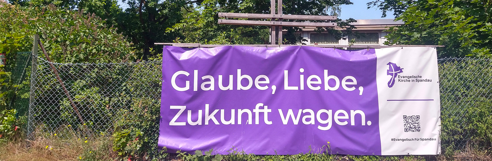 Lila Banner "Glaube, Liebe, Zukunft wagen." an Zaun