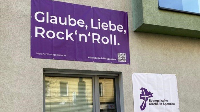 Lila Banner am Gebäude: Glaube, Liebe, Rock'n'Roll.