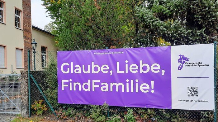 Lila Banner am Zaun: Glaube, Liebe, FindFamilie!