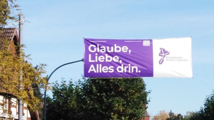 Lila Banner über die Straße gespannt: Glaube, Liebe, Alles drin.