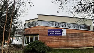 Außenansicht der Kita mit Banner "Glaube, Liebe, Zusammenhalt"
