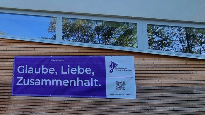 Lila Banner am Zaun: Glaube, Liebe, Zusammenhalt