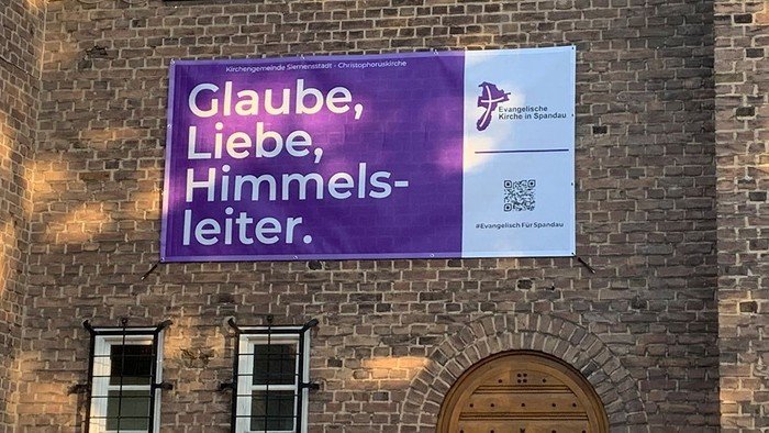Lila Banner am Gebäude: Glaube, Liebe, Himmelsleiter.