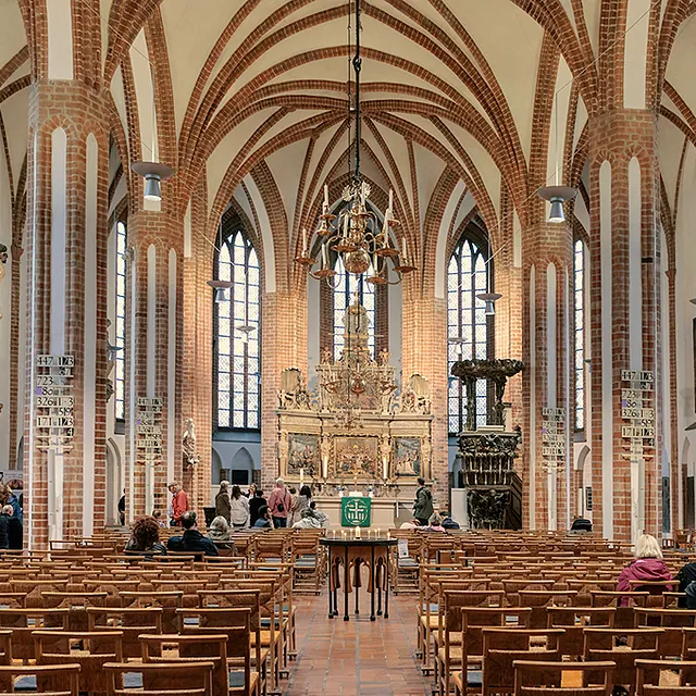 Blick in Kirchraum St. Nikolai, Menschen stehen vor Altar, am Kerzentisch und im Seitenschiff