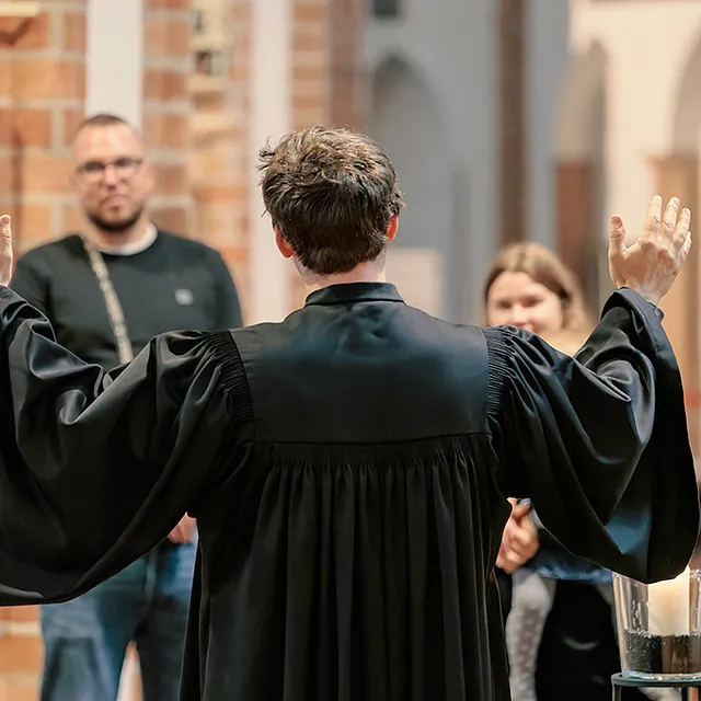 Pfarrer in Taler mit erhobenen Händen vor Taufgesellschaft