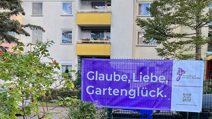 Lila Banner an Zaun: Glaube, Liebe, Gartenglück.